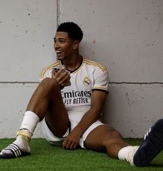 a man sitting on the ground next to a wall holding a cell phone and smiling