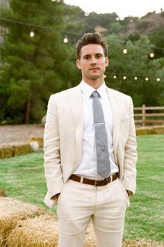 a man wearing a suit and tie standing in front of some hay bales with string lights