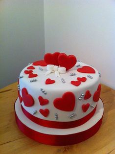 a white and red cake with hearts on it sitting on top of a wooden table