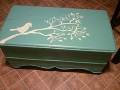 a green box with a white bird painted on it's lid sitting on the floor