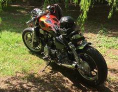 an orange and black motorcycle is parked in the grass near some trees on a sunny day