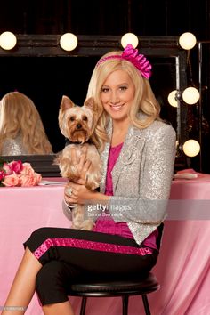 a woman sitting at a table holding a small dog in her lap and posing for the camera