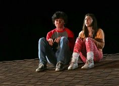 two young people sitting on the roof of a house looking at something in the distance