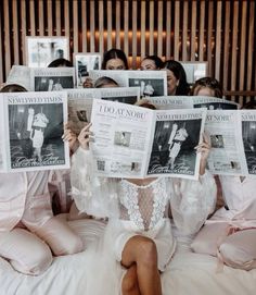 a group of women sitting on top of a bed holding up newspapers in front of their faces