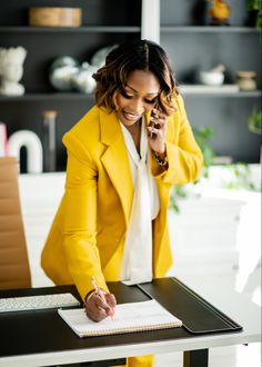 a woman sitting at a table talking on her cell phone and writing in a notebook