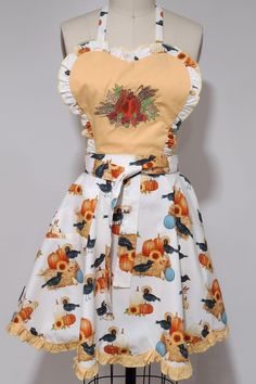 an apron dress with pumpkins and birds on it, sitting on a mannequin