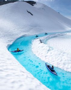 two people are kayaking down a blue stream in the middle of snow covered mountains