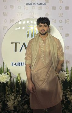 a man standing in front of a sign with flowers on it's side and wearing a tan outfit