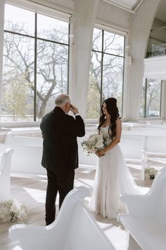 a bride and groom standing in front of white chairs