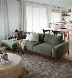 a man sitting on top of a green couch in a living room next to a window