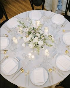 the table is set with white plates, silverware and flower centerpieces on it