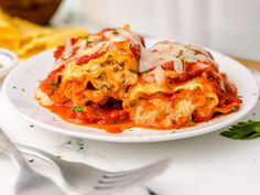 a white plate topped with lasagna covered in tomato sauce and parmesan cheese