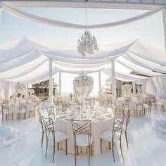 an outdoor wedding setup with white linens and chandeliers on the ceiling, set up for a formal function