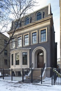 a large gray brick house with black gate and snow on the ground in front of it