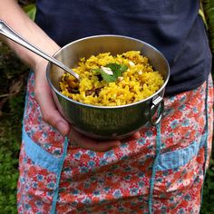 a person holding a bowl of food with a spoon in their hand and wearing an apron