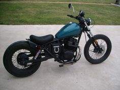 a blue motorcycle parked on top of a cement floor next to grass and trees in the background