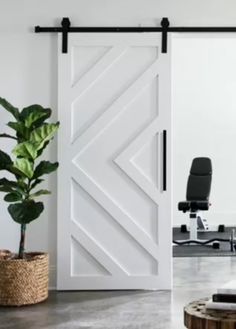 an open white barn door in the middle of a room with a chair and potted plant