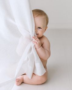 a baby sitting on the floor holding onto a white curtain