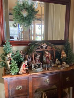 a christmas scene on top of a wooden dresser in front of a mirror with wreaths and figurines