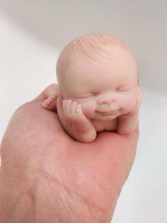 a hand holding a small baby doll in it's right hand, with its eyes closed