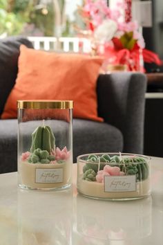 two glass vases filled with plants sitting on top of a white table next to a couch