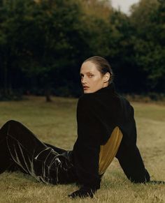 a woman laying on the ground wearing black and brown clothes with trees in the background