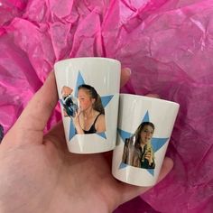 two coffee mugs with pictures of women on them are held in front of pink tissue paper