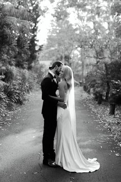 a bride and groom kissing on the road in front of some trees at their wedding