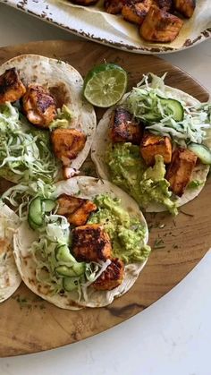 chicken tacos with guacamole and lime wedges on a cutting board