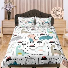 a bed with dinosaurs on it in a room next to a wooden table and chair