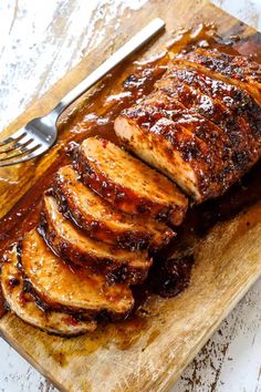 sliced pork on a cutting board with bbq sauce over it and a fork next to it