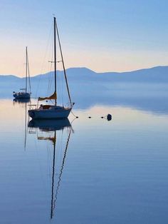 two sailboats floating in the water with mountains in the backgrounnds