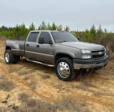 a silver truck parked on top of a dirt road in the middle of a field