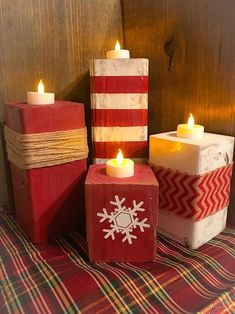 three red and white boxes with candles in them on a plaid tablecloth covered surface