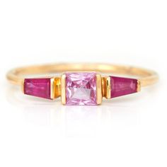 This gorgeous pink Sapphire and tapered Ruby ring reminds of Christian Lacroix's wonderful use of these two colors. The lively pink sapphire is embraced by two extraordinary rubies. The contrast of colors between the two gemstones make them more vivid together that apart.  Hand forged in 18k yellow gold.  For more info Pink Multi-stone Sapphire Ring In Fine Jewelry Style, Pink Multi-stone Sapphire Ring, Fine Jewelry, Pink Multi-stone Sapphire Ring, Pink Sapphire Ring Fine Jewelry, Elegant Pink Multi-stone Sapphire Ring, Pink Ruby Rings With Multi-stone Detail, Pink Ruby Ring With Center Stone Fine Jewelry, Pink Ruby Gemstone Ring For Anniversary, Anniversary Pink Ruby Ring With Center Stone