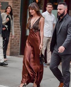 a woman in a brown dress is walking down the street with a man wearing a suit and tie