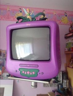 a purple tv with tinkerbells on top sitting in a child's room