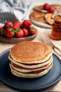 stack of pancakes with syrup and strawberries in the background