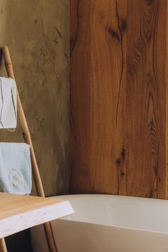 a wooden ladder leaning against a wall next to a bathtub with towels on it