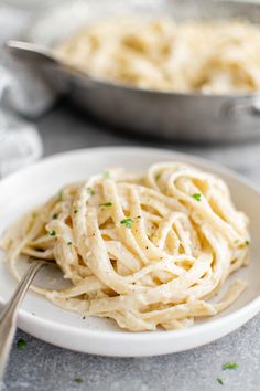 a white plate topped with pasta and parmesan cheese sauce next to a skillet