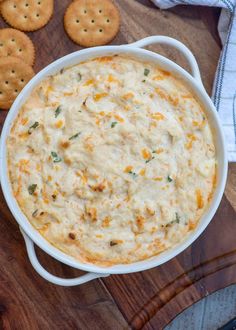 a casserole dish filled with cheese and crackers on a cutting board next to some crackers