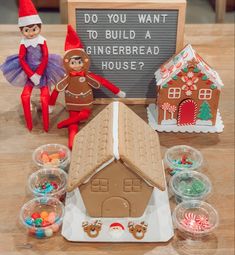 gingerbread house with two elfs next to it and candy in plastic bowls on the table