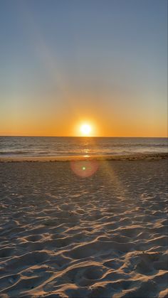 the sun is setting over the ocean with waves in the foreground and sand on the beach