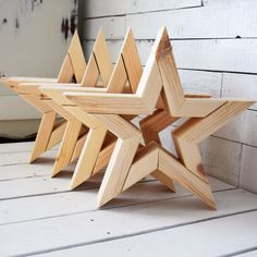 three wooden star shaped objects sitting on top of a white wood floor next to a brick wall