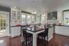 a large kitchen with white cabinets and black counter tops, hardwood flooring, and an island in the middle