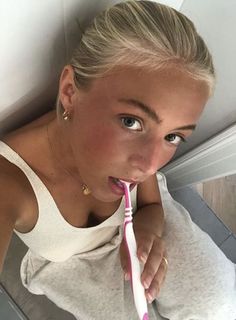 a woman brushing her teeth with a pink toothbrush