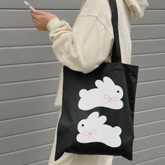 a woman holding a black bag with two white rabbits on it and a cell phone in her hand