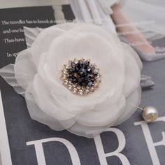 a white flower on top of a black and white brooch with pearls in the center