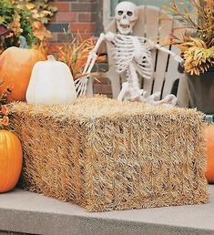 a fake skeleton sitting on top of hay bales next to pumpkins and other decorations