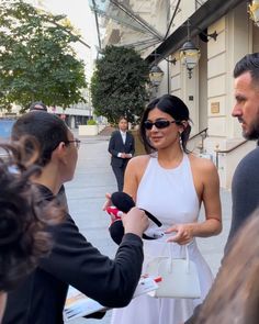 a woman in a white dress is talking to two men and holding a small handbag